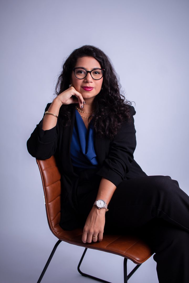 Anniele Costa, advogada, sentada em uma cadeira de couro, de blazer preto, olhando para a câmera.